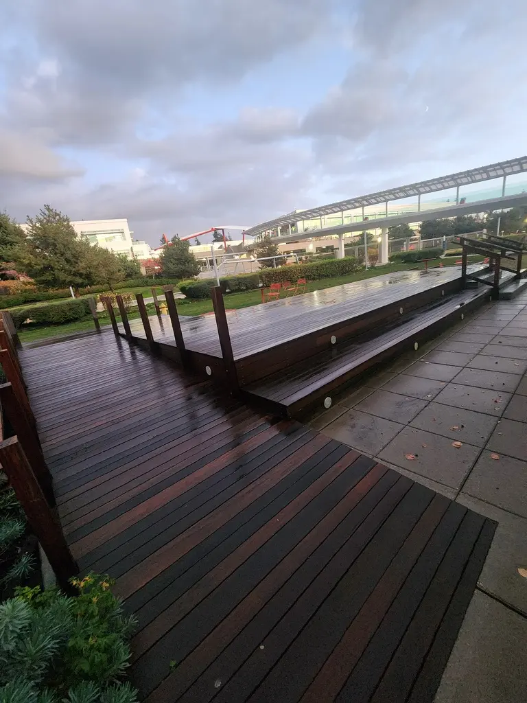 Raised deck platform and wide steps before refinishing, boards wet and dark under a cloudy sky