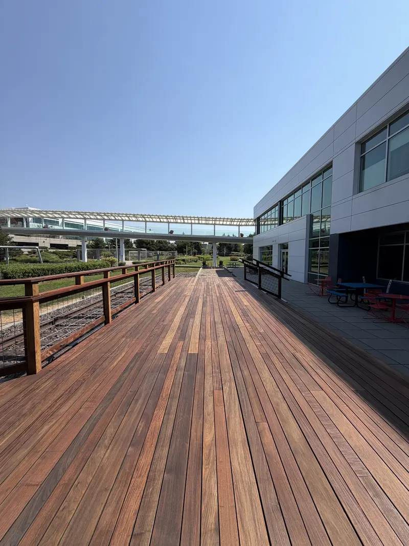 Long run of refinished deck boards beside the office building, railing on the left