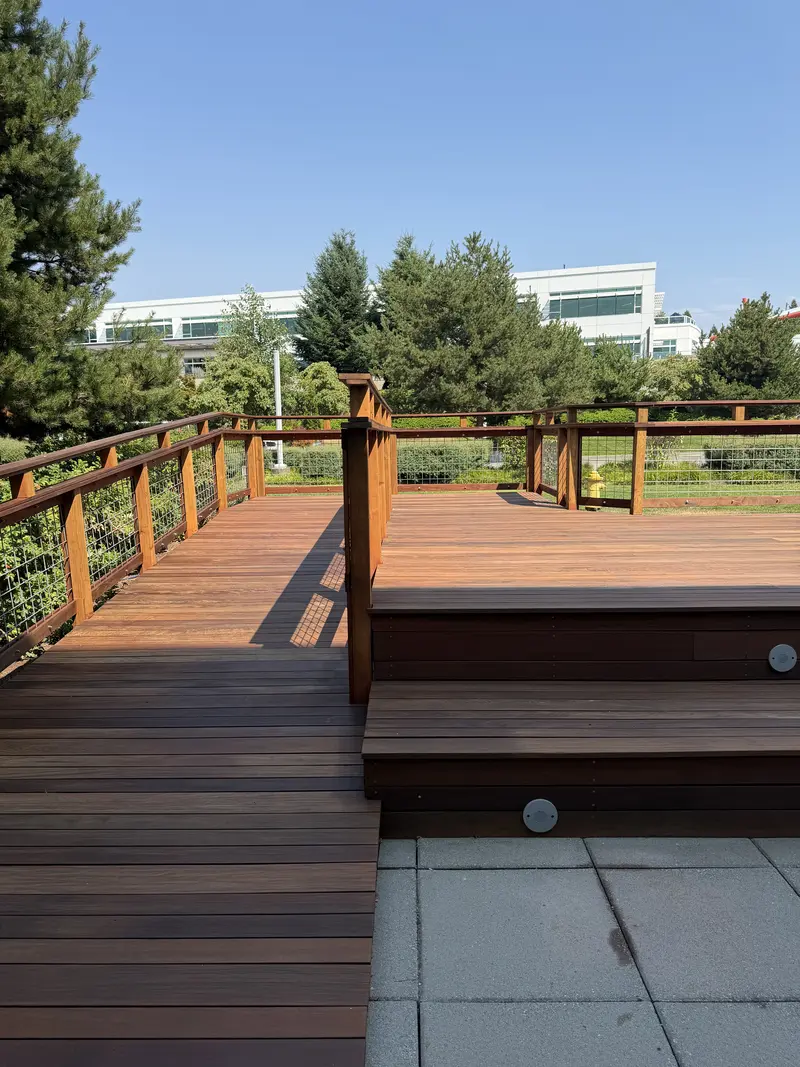 Refinished deck steps and a railing corner post, lawn and office buildings behind