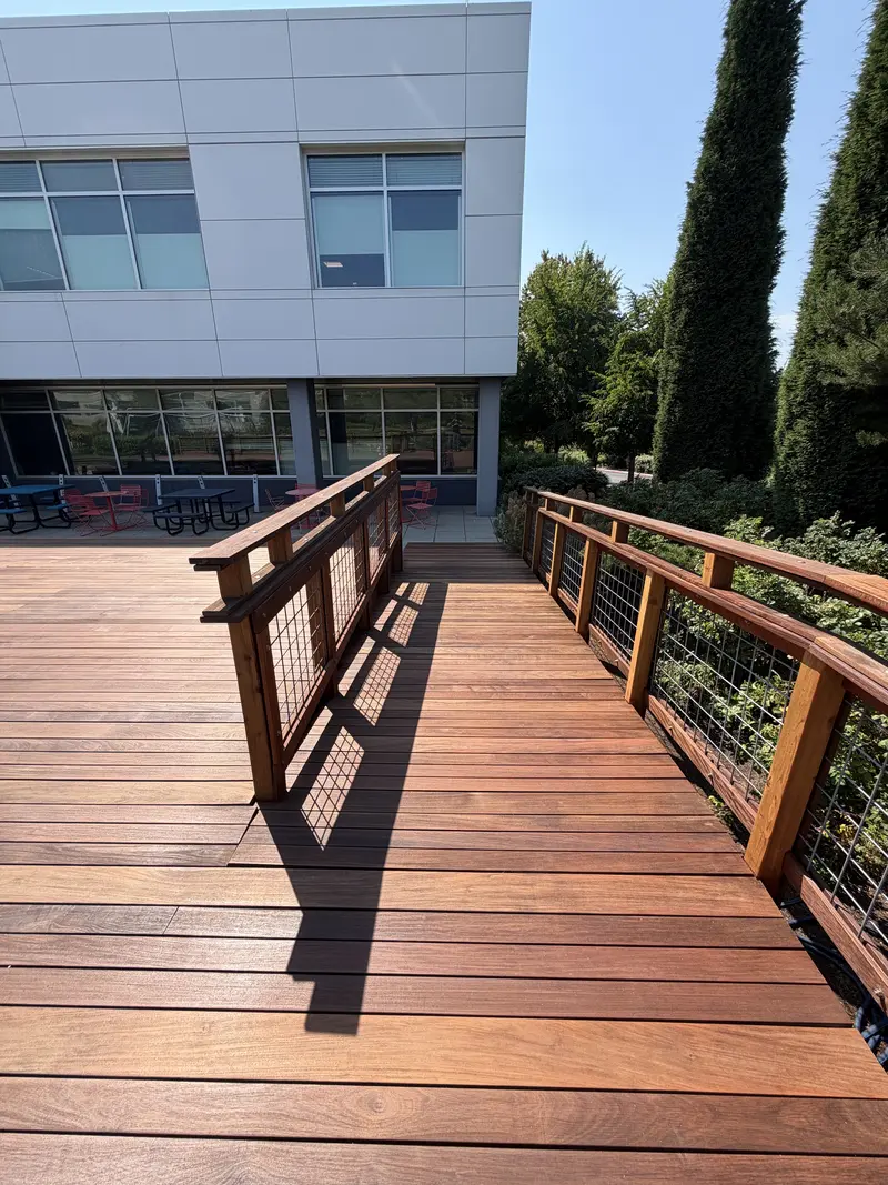 Refinished deck walkway with wood and wire railing leading to the office building patio