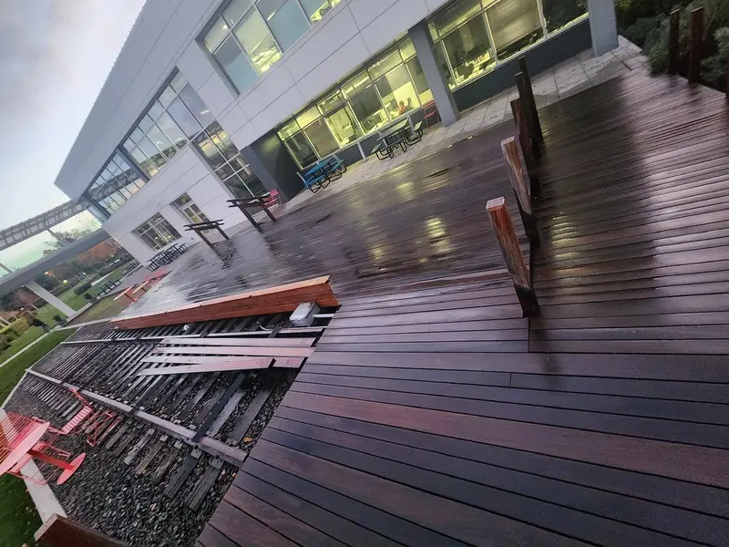 Deck before refinishing, dark wet boards and wide steps along the rail-line side of an office building