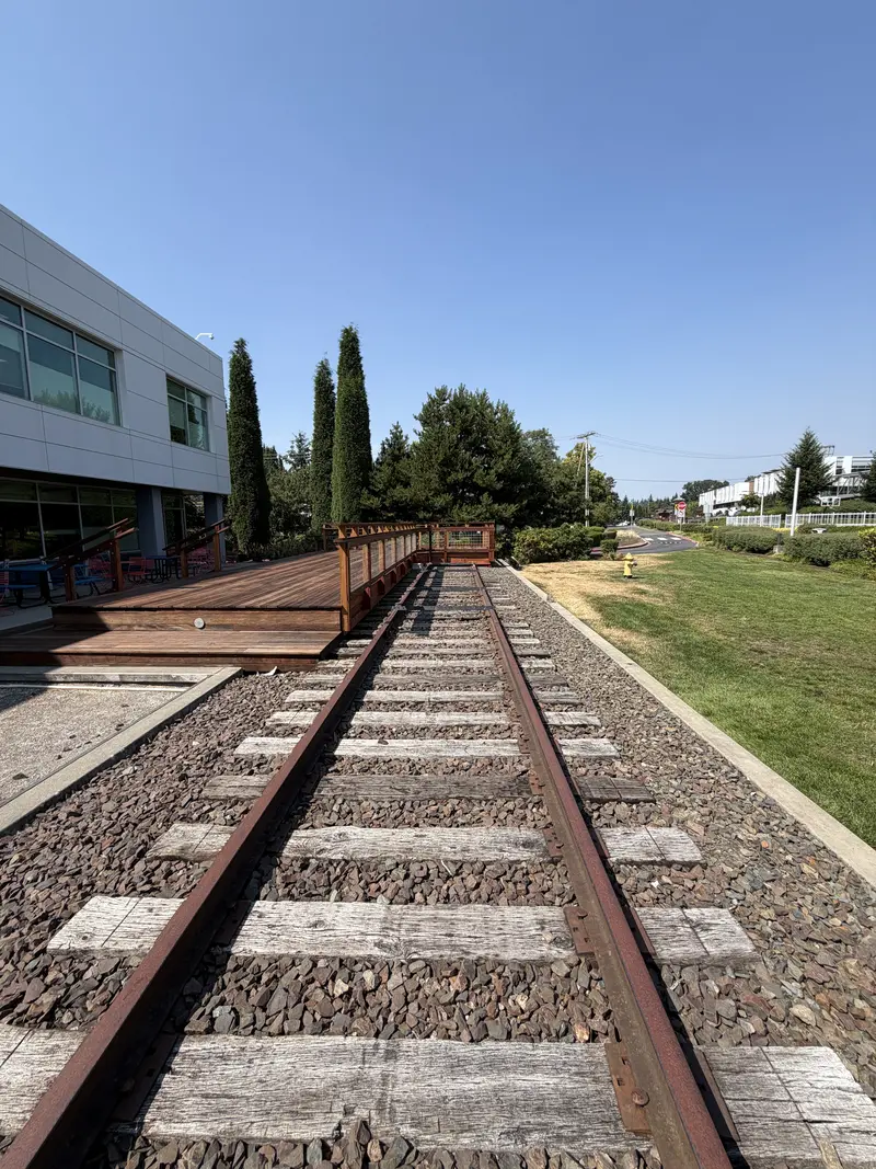 Refinished deck running beside the old railroad track and gravel bed, office building on the left