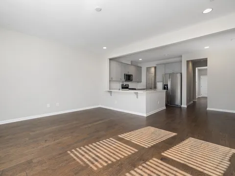 Vacant apartment living room with light gray walls, dark wood floors and an open kitchen with gray cabinets and stainless appliances