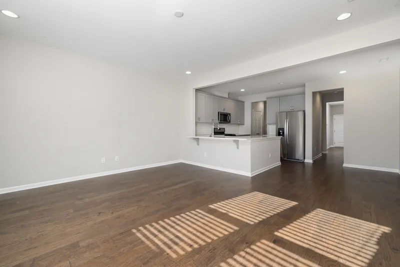 Vacant apartment living room with light gray walls, dark wood floors and an open kitchen with gray cabinets and stainless appliances