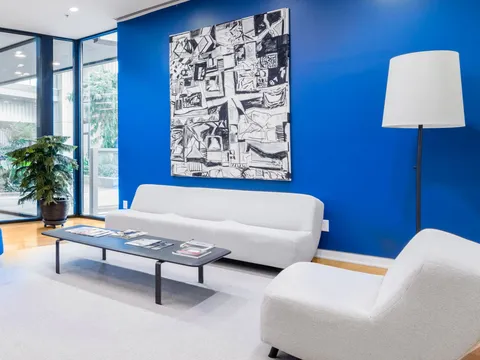 Office lobby with a deep blue painted accent wall behind a white sofa, a large black and white artwork, a floor lamp and a low coffee table