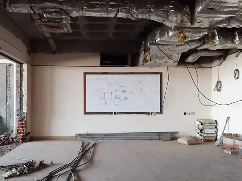 Stripped office floor mid renovation with exposed insulated ductwork, hanging wiring, a whiteboard and metal studs on the floor