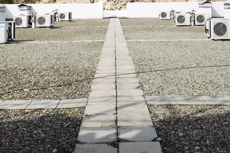 Gravel ballasted flat roof crossed by concrete paver walkways, with rows of condensing units along the parapet