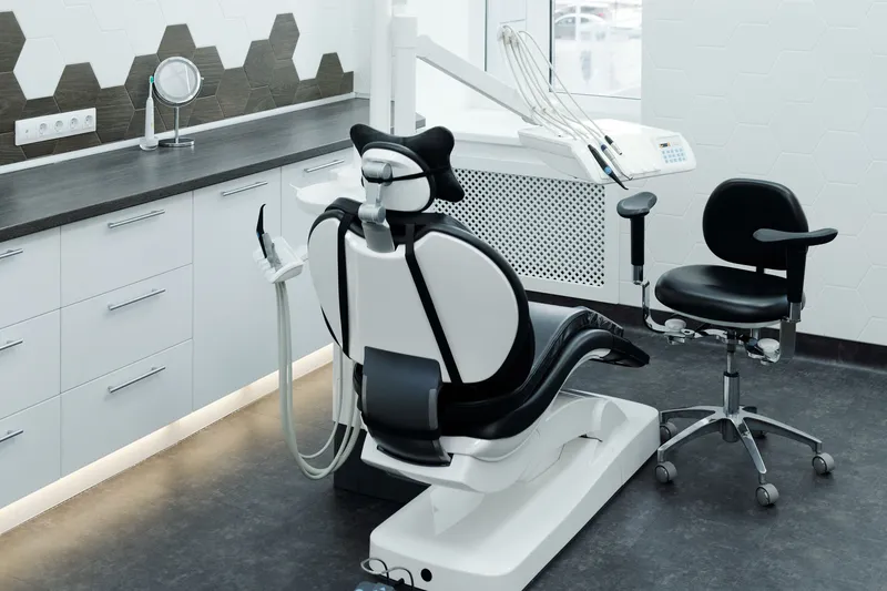 Empty dental operatory with a black and white patient chair, delivery unit, operator stool and white cabinetry