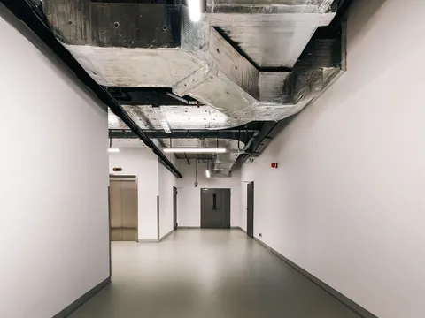 Commercial building corridor with insulated ductwork, cable trays and linear lights overhead, steel service doors and an elevator