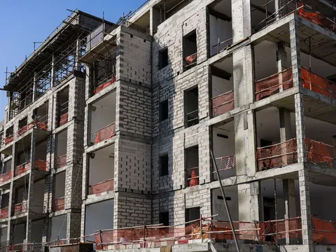 Multi storey apartment building under construction with concrete frame, block infill walls, open balconies and orange safety netting along each floor edge