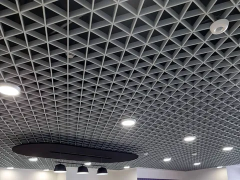 Open cell triangular grid ceiling with round LED downlights, a ceiling mounted sensor, a dark suspended acoustic panel and three black pendant lights