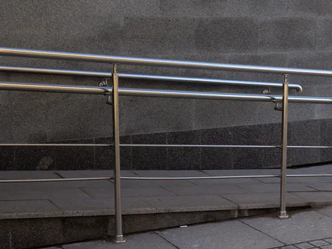 Concrete ramp with stainless steel double handrails running along a gray granite wall beside a paved sidewalk