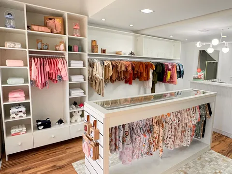 Bright boutique with white built-in shelving and hanging rails, a glass topped display island with a clothes rail beneath, recessed ceiling lights and a wood look floor