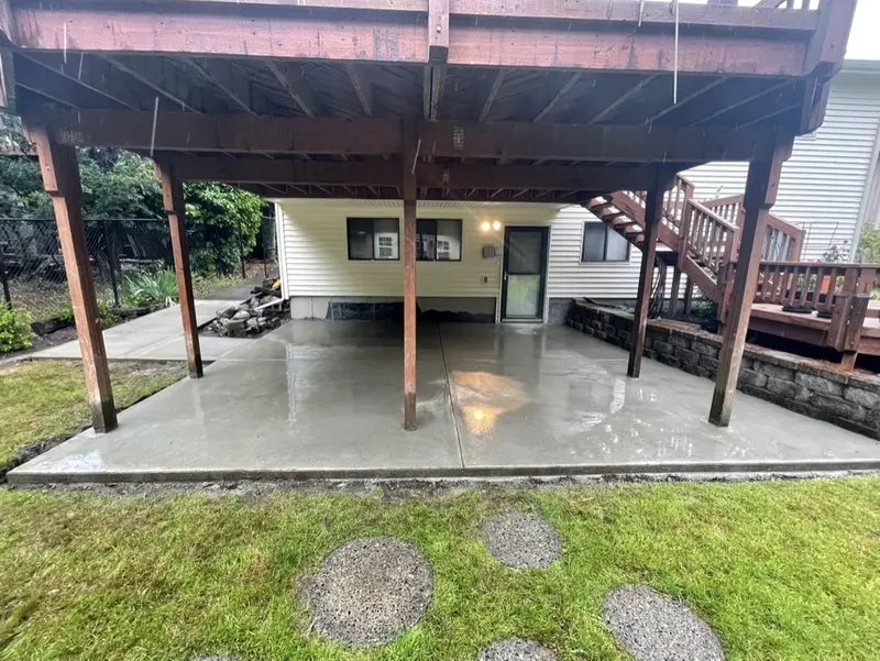 Finished concrete patio under an upper deck, with stepping stones leading across the lawn to it