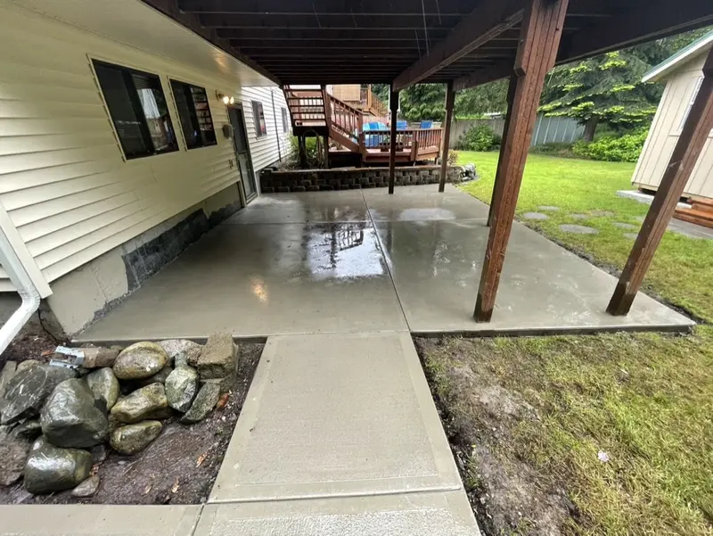 Concrete walkway leading from the lawn to the patio under the deck, beside river rock