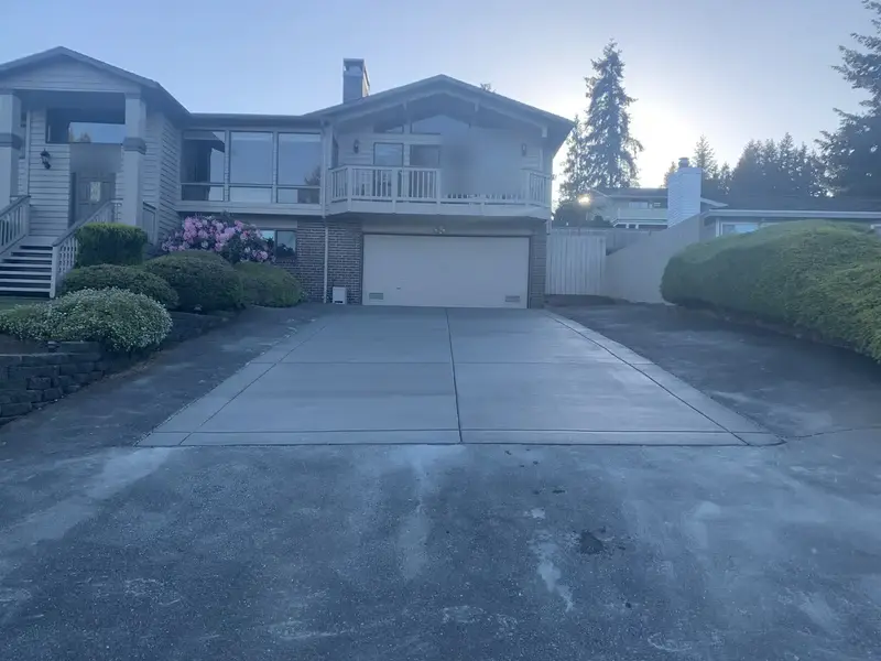 New concrete driveway leading up to a two-story house and its garage door