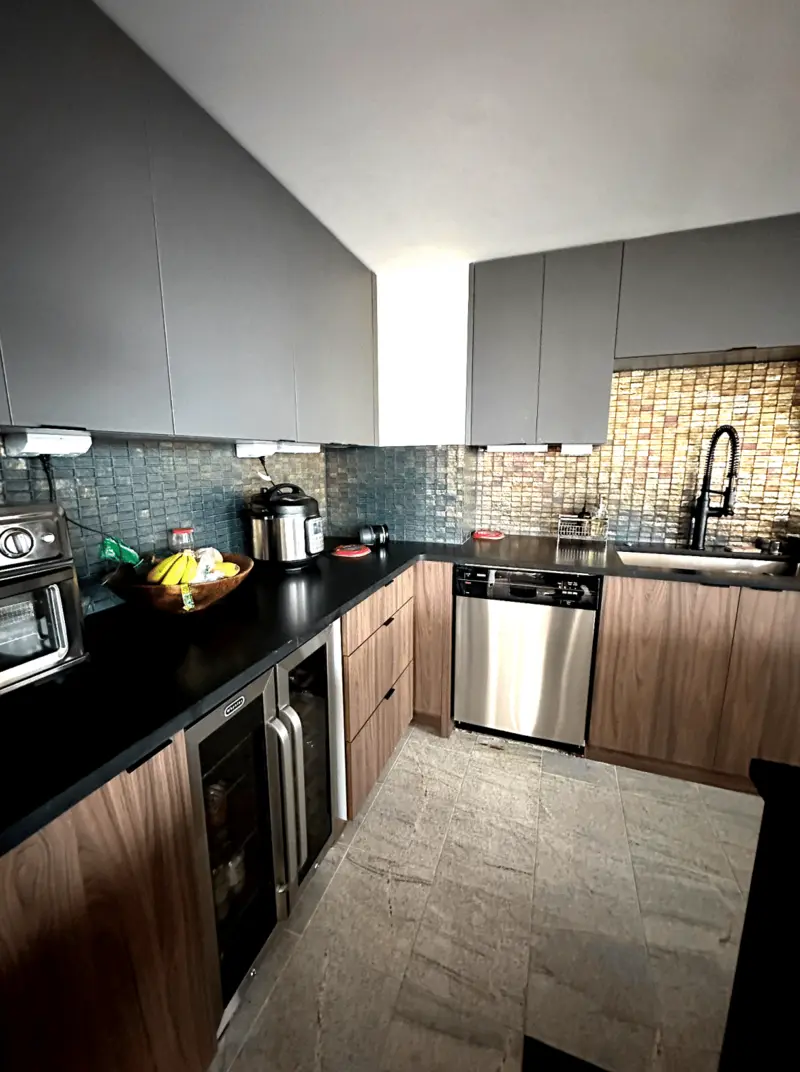 Kitchen run with black counters, wood-grain base cabinets, wine refrigerators and an iridescent mosaic backsplash