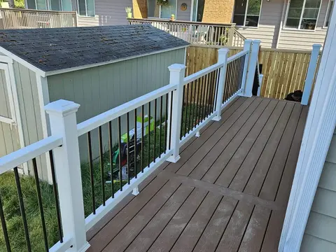 Brown composite deck walkway along a house with a white railing and black balusters in Seattle, WA