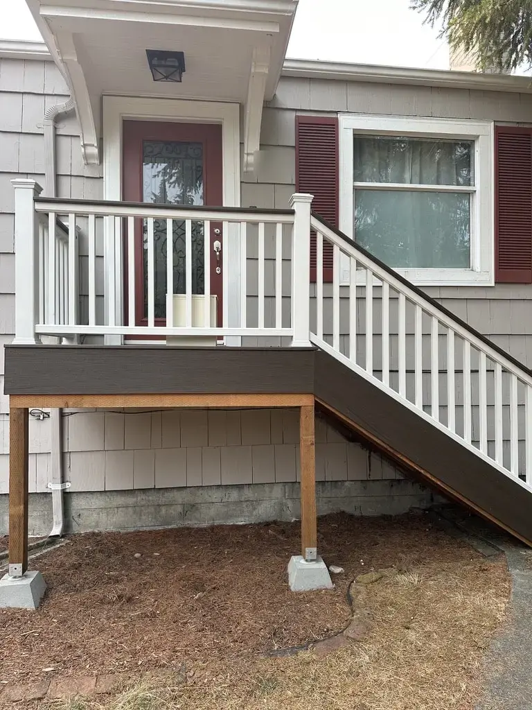 Front entry landing with a white railing and stair in front of a red door under a small roof