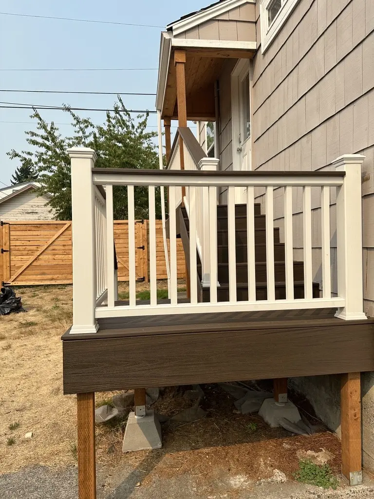Landing with white railing panels on dark brown fascia, standing on wood posts above gravel
