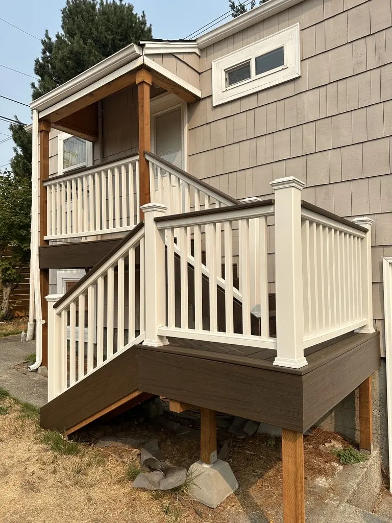Raised rear landing with a white railing and a stair turning down to the yard beside a shingled wall