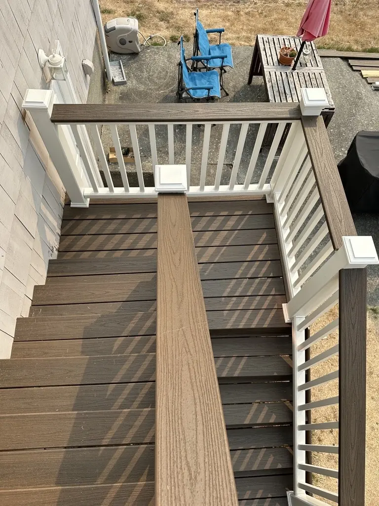 Looking down a stair with dark brown treads, white balusters and a wood-grain cap rail
