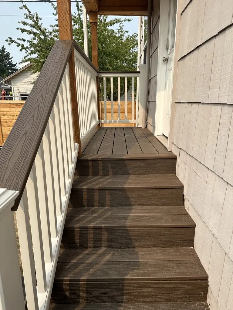 Stair climbing along shingled siding to a covered landing, with a white railing and wood cap rail