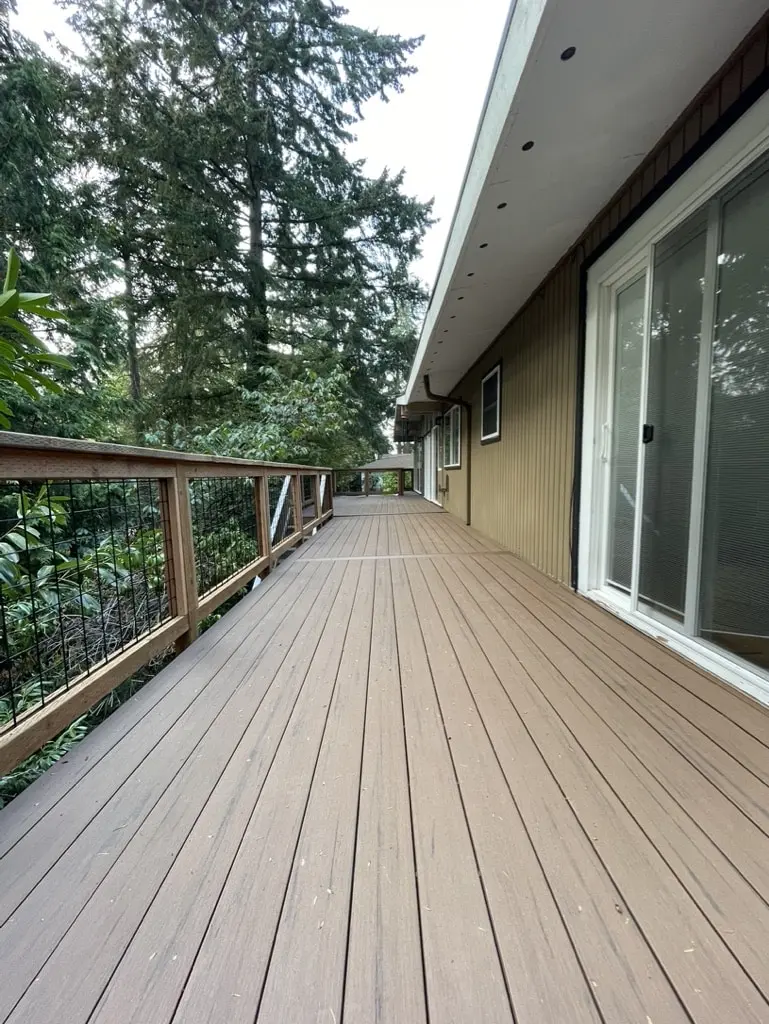 Long rebuilt deck with gray-brown boards running past sliding doors, with a wood and metal railing