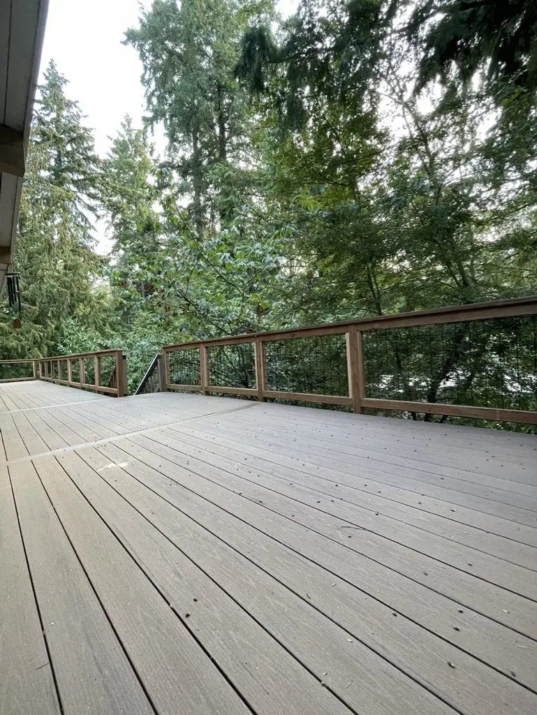 Wide rebuilt deck with new boards and a railing facing tall evergreen trees