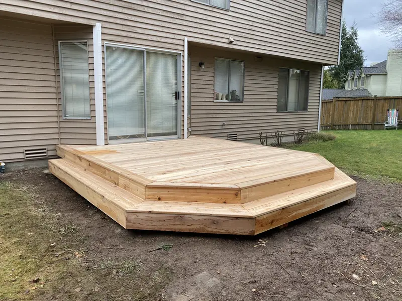 Low wood deck with angled corners and a perimeter step on fresh soil behind a house