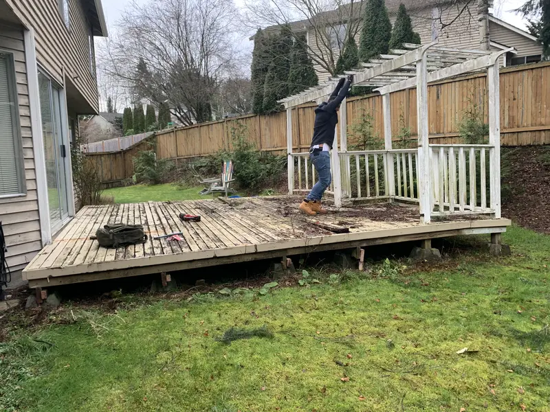 Old low wood deck with a white pergola and railing being taken apart behind a house