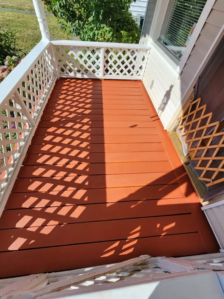 Porch deck floor freshly painted red inside a white lattice railing beside the house