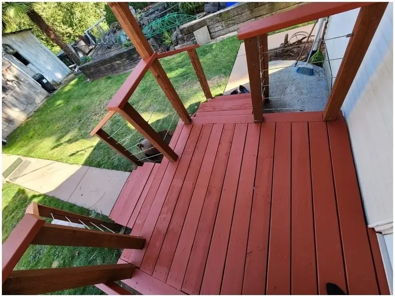 Side entry deck painted red, with red posts, top rails and wire infill, steps down to the yard