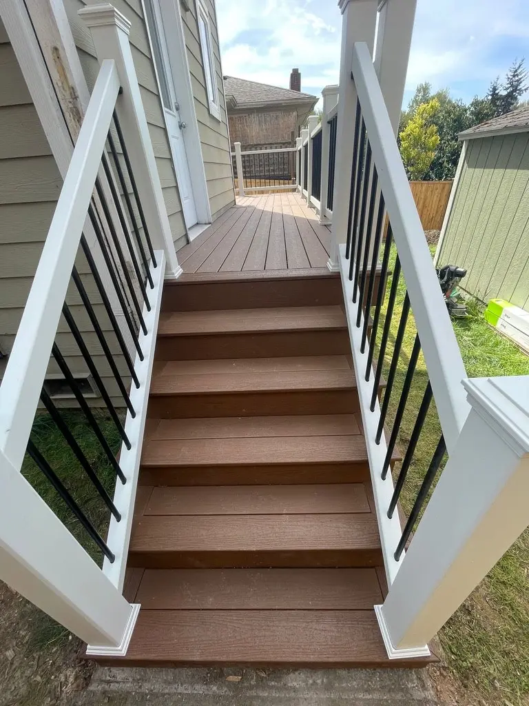 Deck stair seen from the yard, with white railings and black balusters on both sides