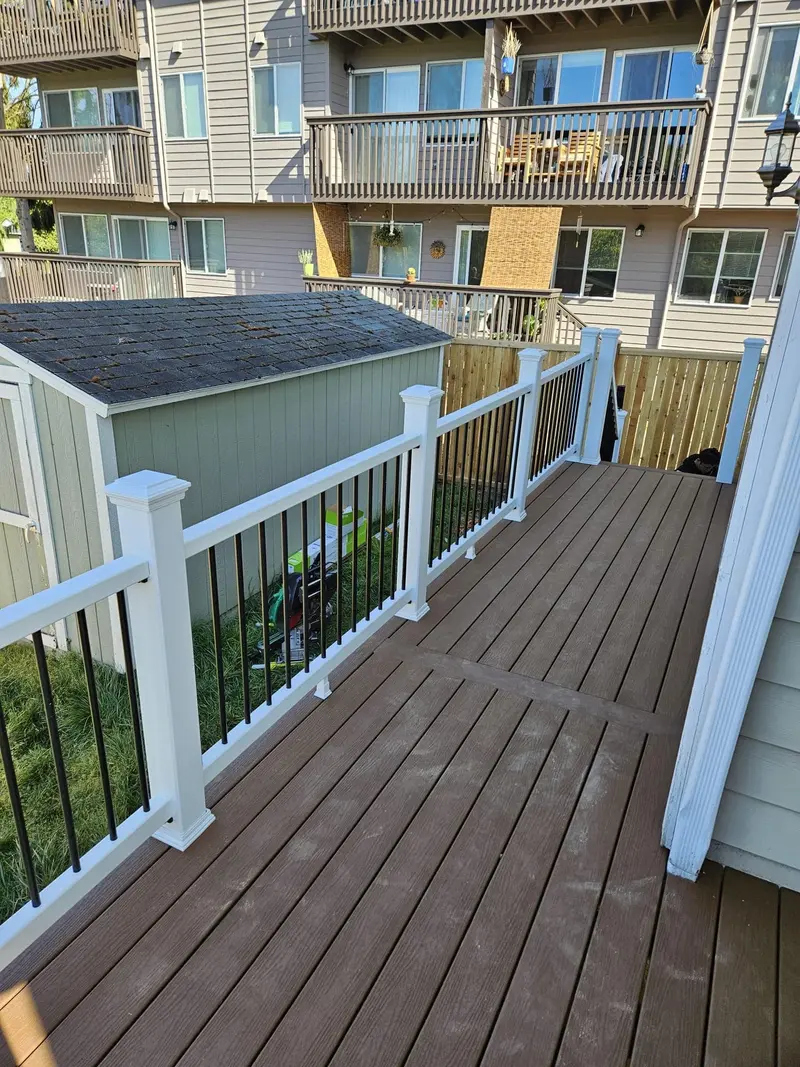 Narrow section of the deck running along the house siding with a white and black railing