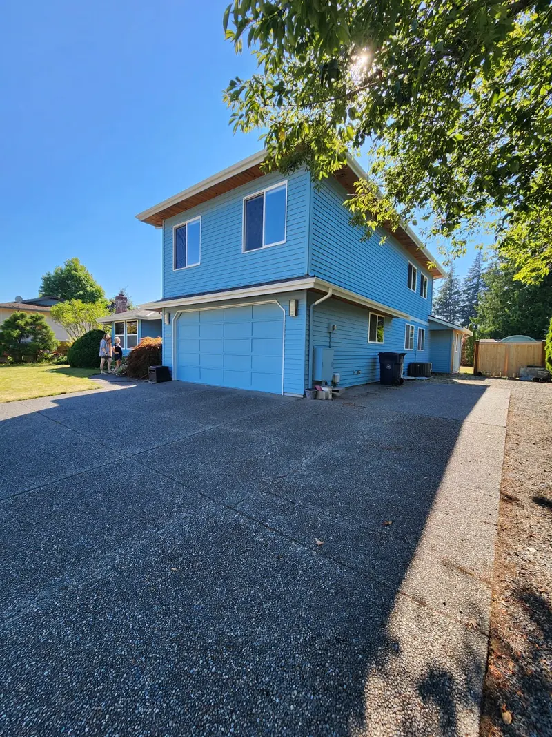 Two-story garage painted blue with a blue garage door and white trim at the end of the driveway