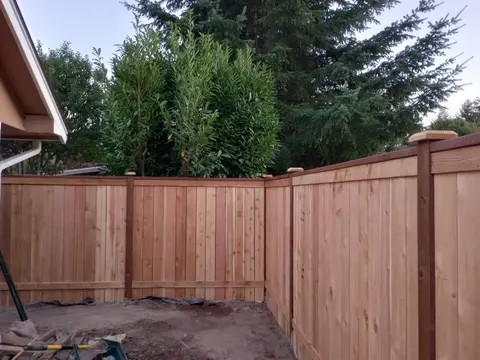 Corner of a new wood privacy fence meeting the house with a cap board and post caps in Auburn, WA