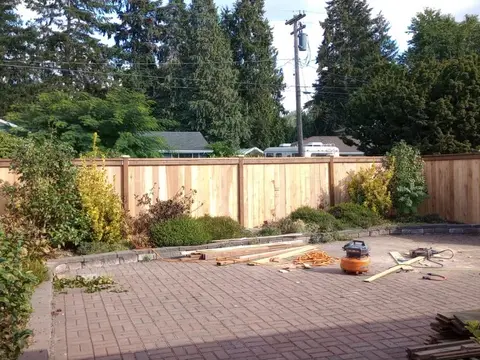 New board fence closing in a backyard paver patio with evergreen trees behind it in Auburn, WA