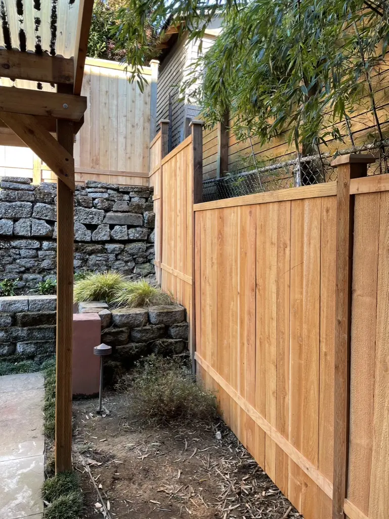 New cedar fence panel beside a pergola post, with a stacked stone wall and planting behind it