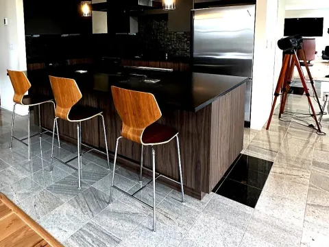 Kitchen in Seattle, WA with a gray stone look tile floor, a black island and wood bar stools