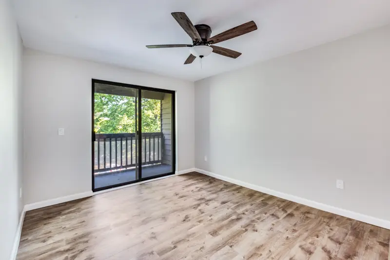 Bedroom with plank floor, ceiling fan and a sliding door to the balcony