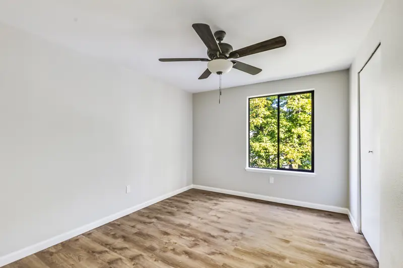 Second bedroom with plank floor, ceiling fan and a window