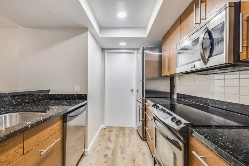 Galley kitchen with plank floor running between wood cabinets and stainless appliances