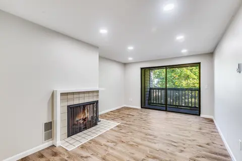 Empty living room with light wood-look plank floor meeting a tiled fireplace hearth