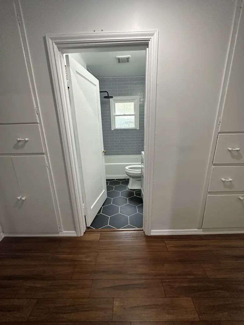 Plank floor ending at a bathroom doorway with black hexagon tile beyond