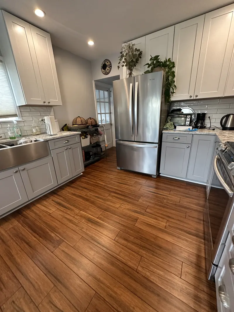 White kitchen with gray lower cabinets and a stainless refrigerator on a dark wood-look plank floor