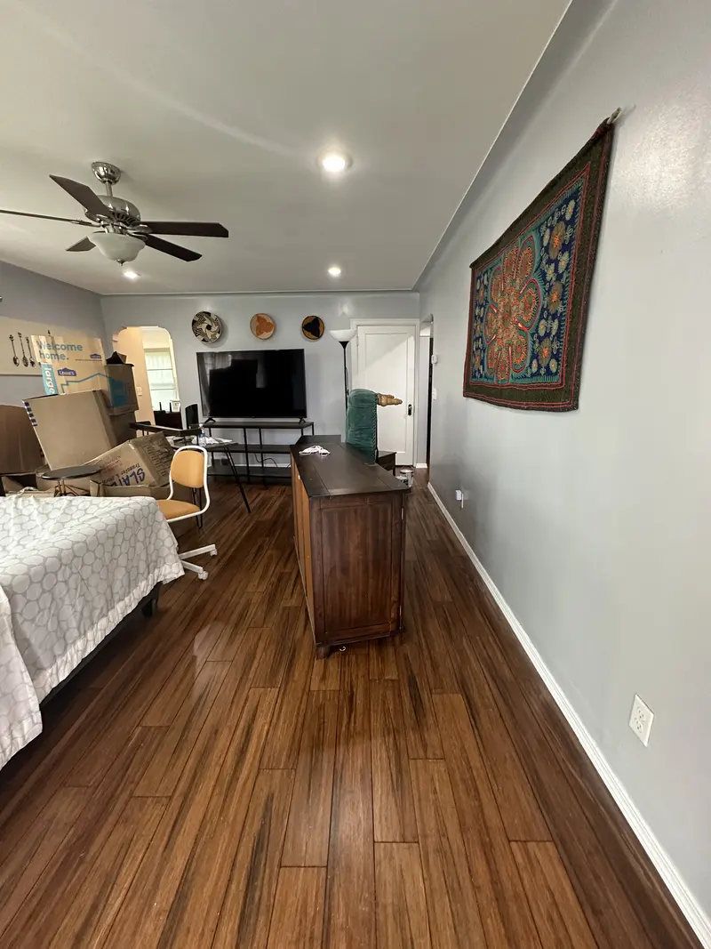 Bedroom with a dark wood-look plank floor, ceiling fan and a long view to the living area