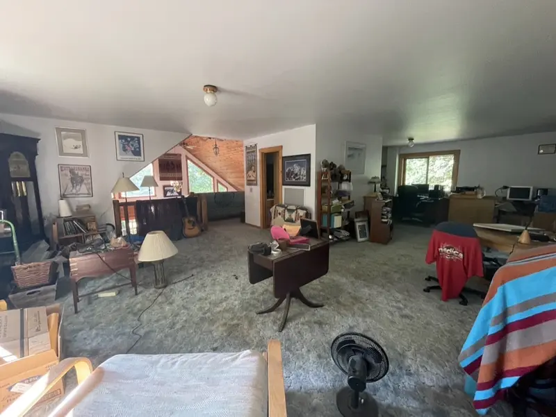 Living area with carpet and furniture under a log stair before the new floor