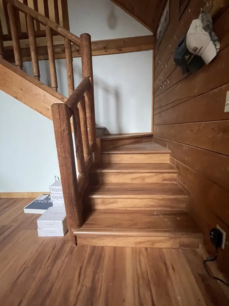 Lower stair flight with new wood-tone treads turning at a landing beside log walls