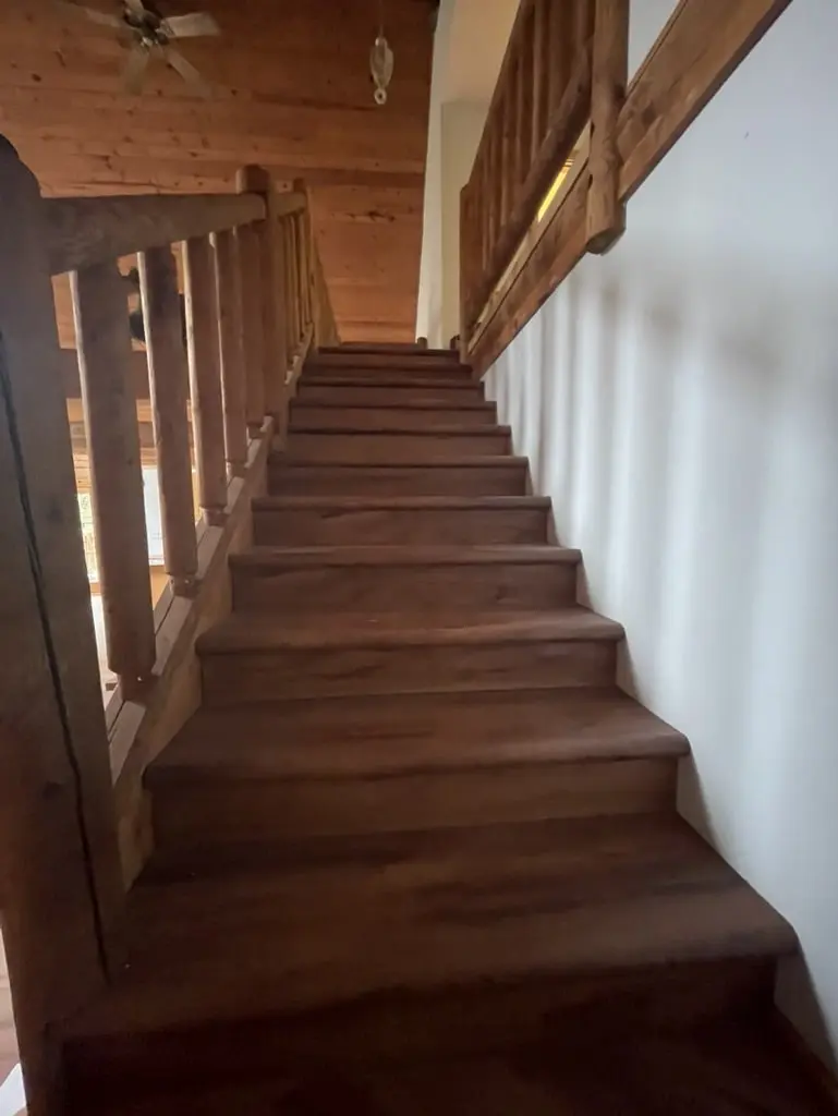Long stair flight with new wood-tone treads and risers beside a log railing
